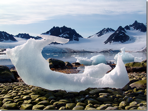 An eroded iceberg on a pebble beach on the Magdalenefjorden (Gully Glacier in background) in Spitsbergen, Svalbard, Arctic Norway  